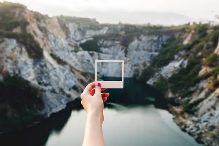 A person holding a square photo frame against a landscape 