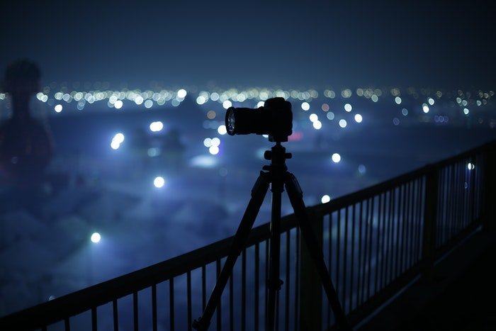 A camera set up on a balcony at night with street lights in the background for Milky Way photography