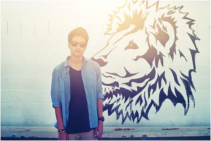 Casual senior photo of a young man posing outdoors in front of a wall