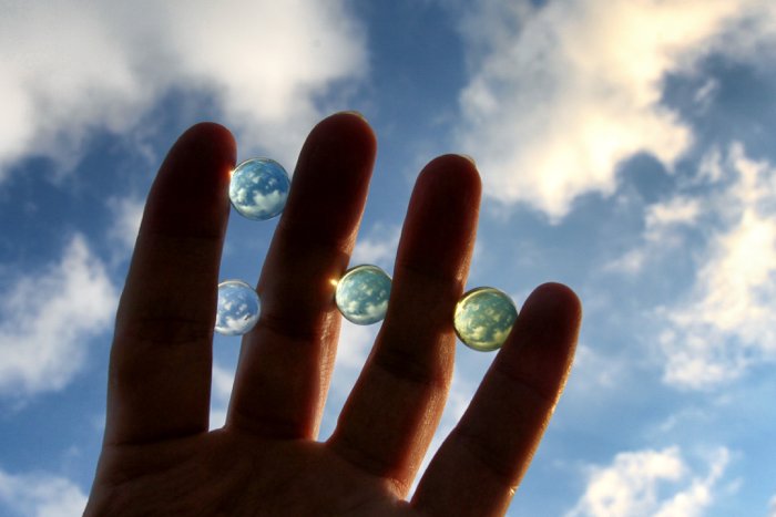 A close up of a hand wirth marbles in between each finger - refracted light photography