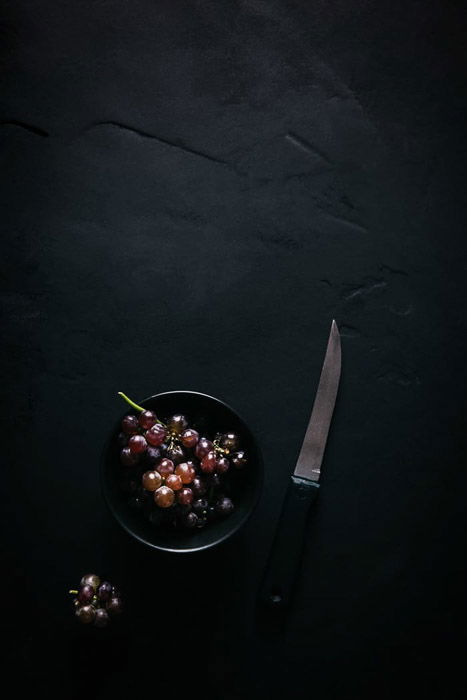 Overhead food shot of grapes in a bowl beside a knife 