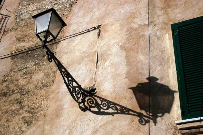 Street photo of a lantern with shadow cast on a stone wall