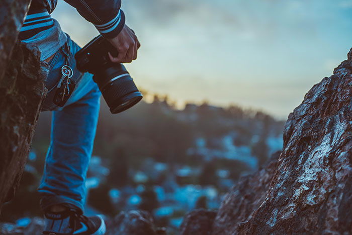 Close up of a solo adventure photographer standing on a rock and holding a dslr camera