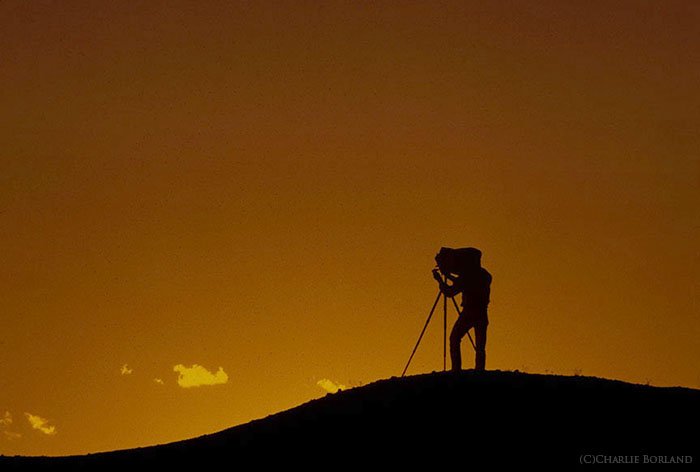 A silhouette of a solo adventure photographer against a sunset sky