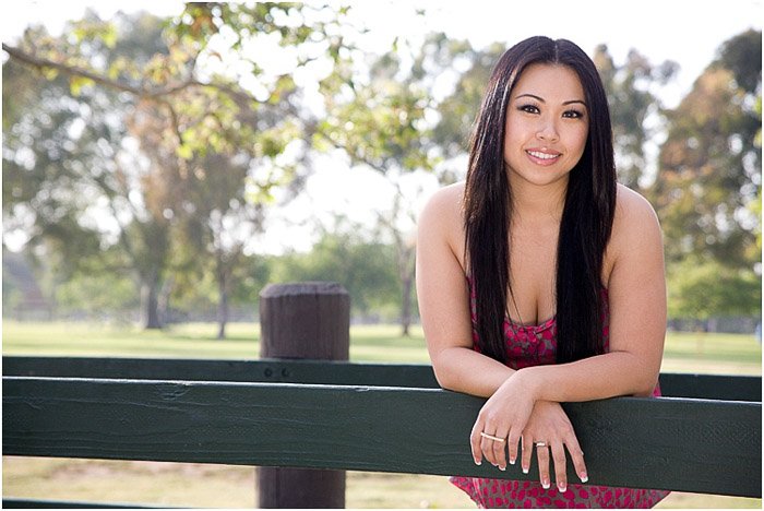 A relaxed and natural senior photography of a brunette girl posing against a fence