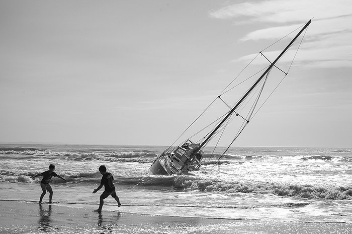 A monochrome shot of kids playing near a boat on New Brighton Beach, New Zealand., black and white photography tips