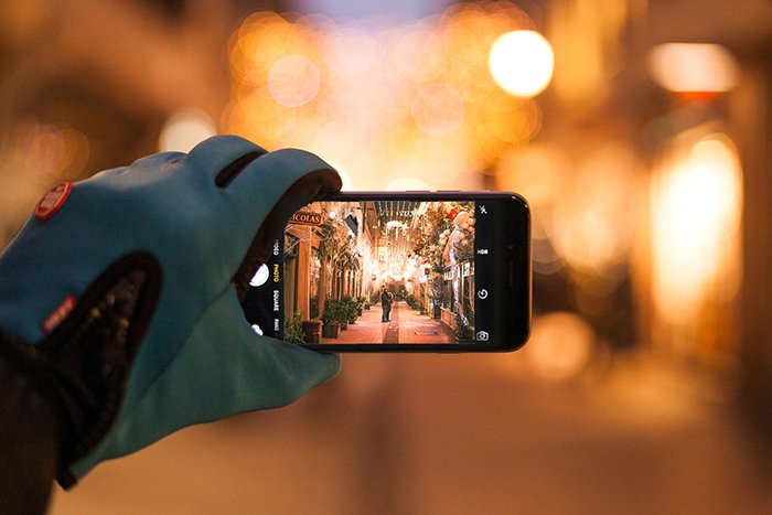 A person taking a smartphone photo of Christmas bokeh lights on a street