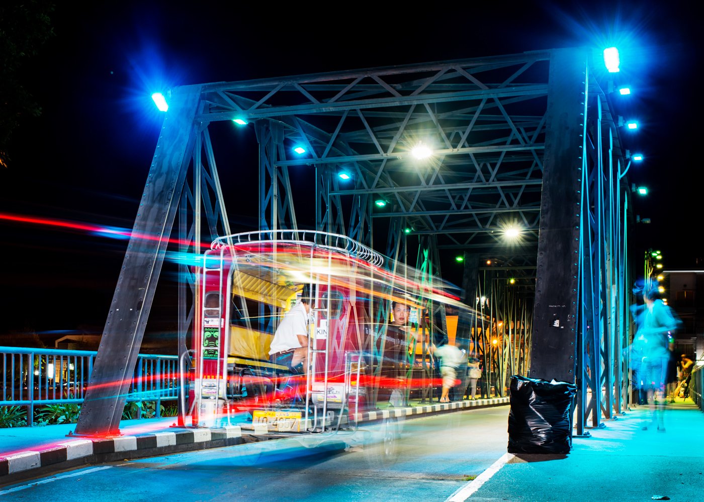 A nighttime long-exposure image of a ghostly figure and train on a bridge