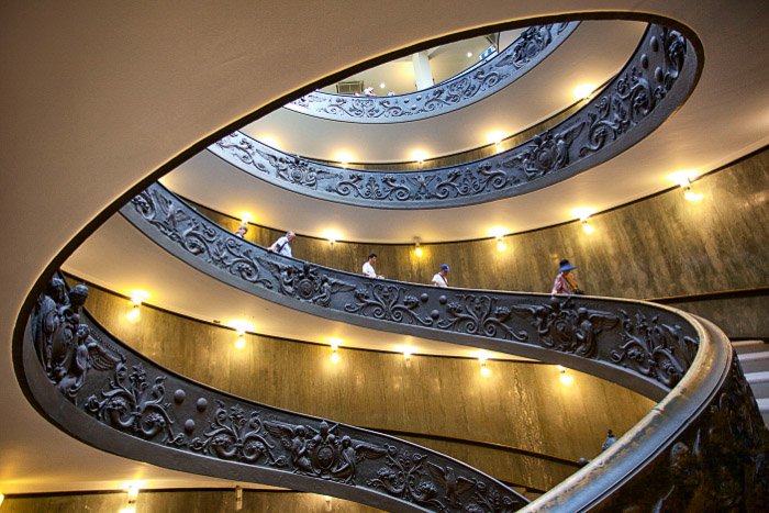 People walking down a spiral staircase in the interior of an impressive building 