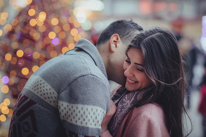 A couple embrace in front of a Christmas tree with bokeh lights background