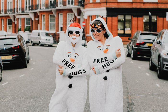 Humorous Christmas portrait of two friends in costume offering free hugs