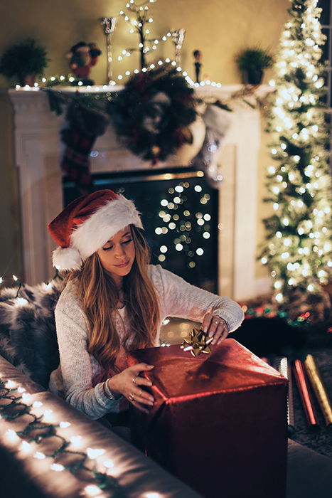 Christmas photo of a woman wrapping gifts on a sofa by the Christmas tree