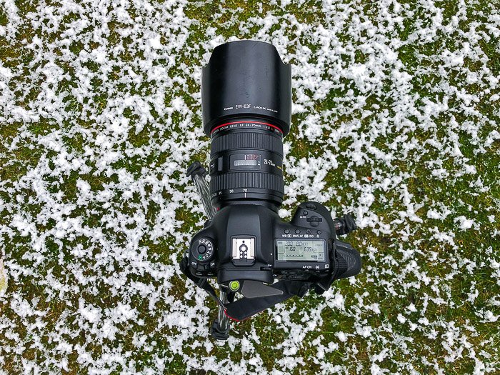 A DSLR with zoom lens resting on snowy grass - stock photography equipment