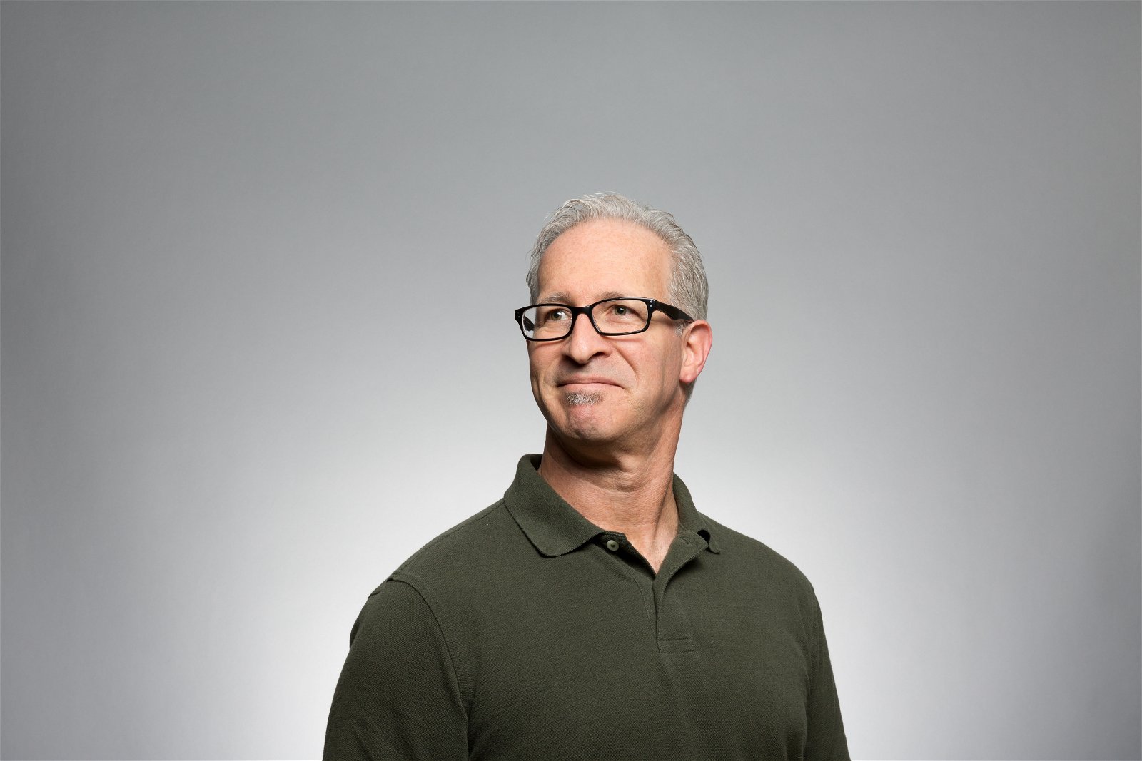 A man with glasses and a green polo shirt looking off to the side for a headshot studio pose
