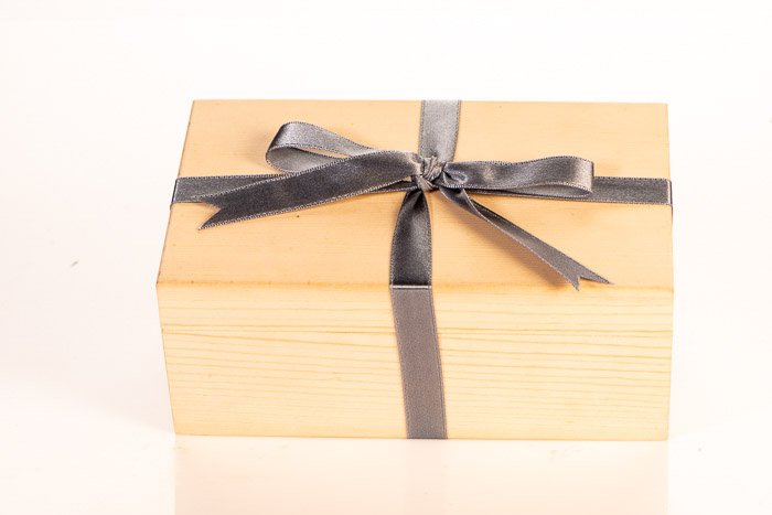 A wooden box wrapped with a grey bow against a white background