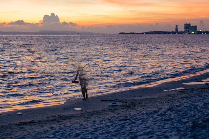 Screenshot showing how to remove people from photographs using a photo of a woman walking on a beach at evening time