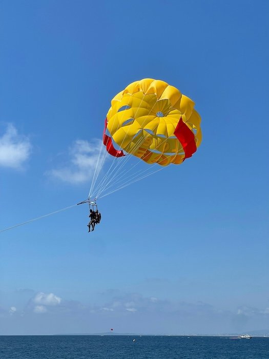 A paraglider sailing over water with a yellow and red parachute against a blue sky show with iPhone photo bursts