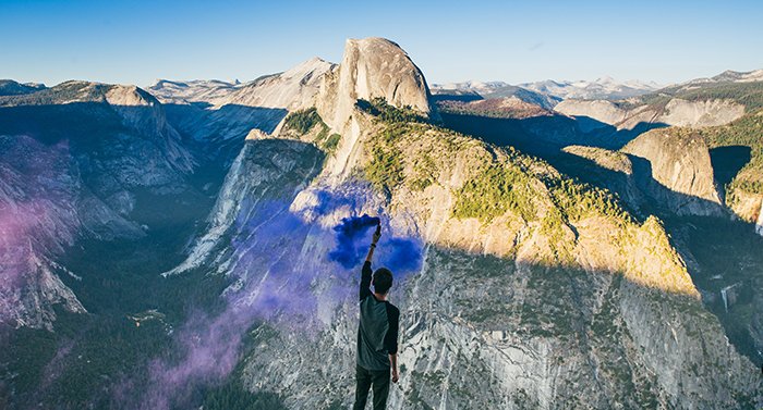 Impressive portrait of a man waving blue smoke grenades in a mountainous landscape
