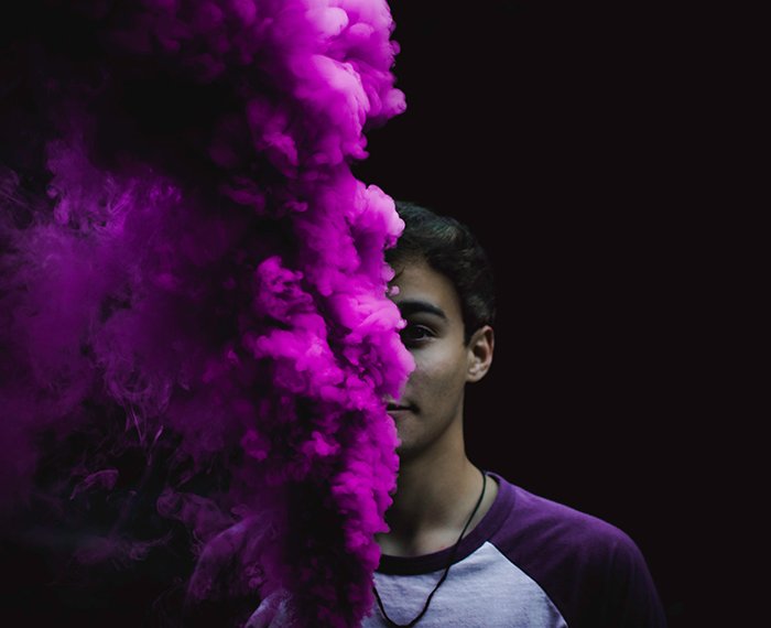 A creative portrait of a man posing in front of a black background with intense pink smoke bomb photography effect