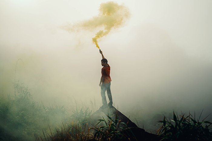 Atmospheric portrait of a man waving smoke grenades in a landscape setting