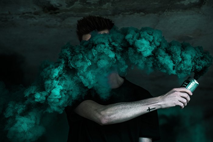 A creative smoke bomb photography portrait of a man holding green smoke grenade near his face