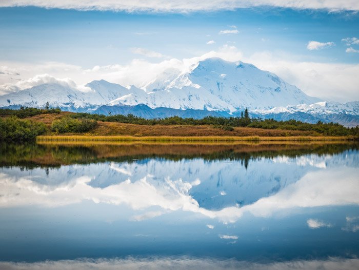 A clear fall landscape shot of snowy mountains reflected in water below