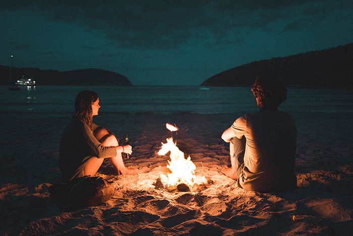 A couple sitting by a bonfire on a beach at night - bonfire pictures