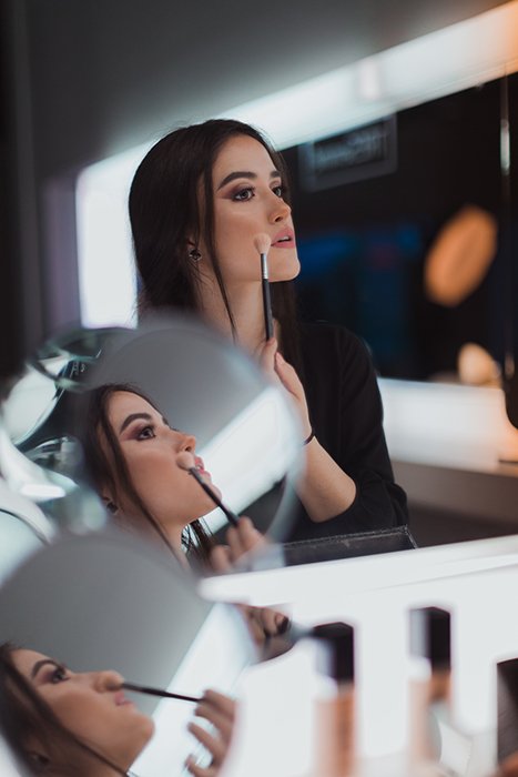 A diptych portrait of a brunette female model reflected in several mirrors while applying make-up 