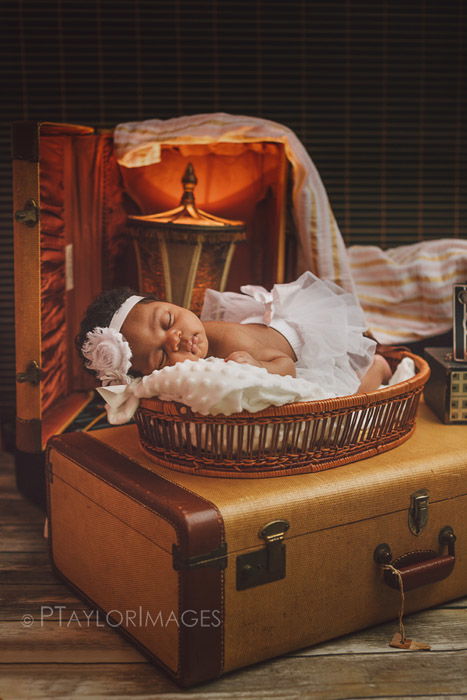 a newborn posed on the top of a suitcase among other newborn photography props