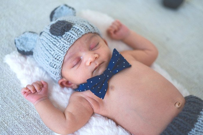 A bare chested newborn in a funny hat and dickie bow as newborn photography props