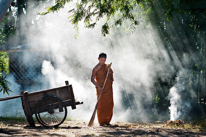 Beautiful rim light portrait of a Buddhist monk sweeping outdoors