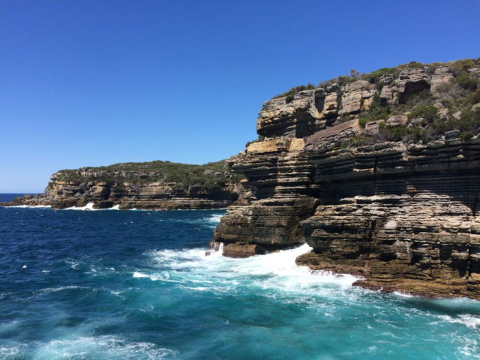 turquoise waters and foamy waves crashing against a rocky cliff face against a bright blue sky - photo editing tips for smartphone photography