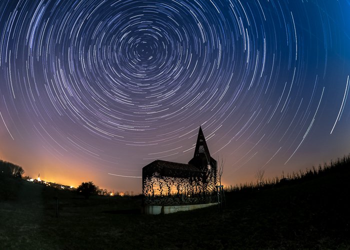 Silhouette of the See Through Church lit warmly from behind, under the star filled night sky