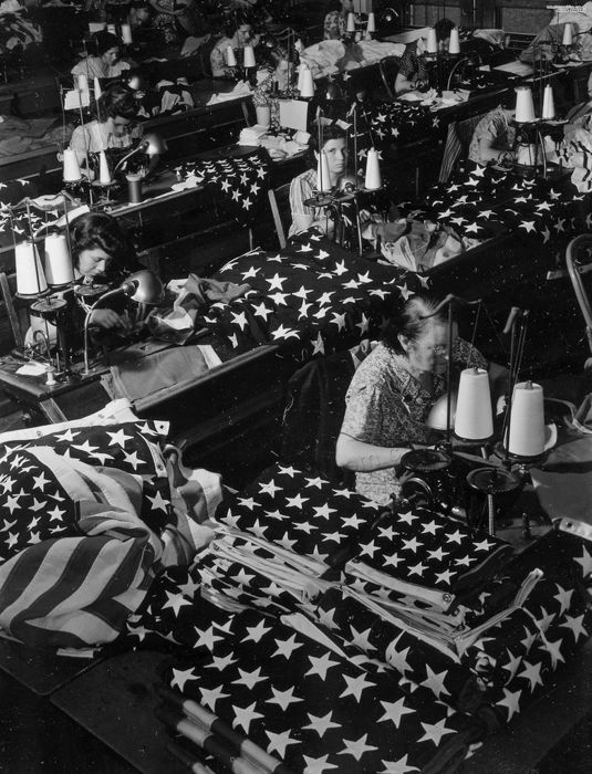 A black and white shot of women sewing american flags by war photographer Margaret Bourke-White