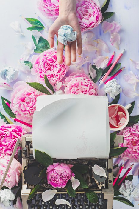 A bright and airy flatlay of pink roses surrounding a typewriter 