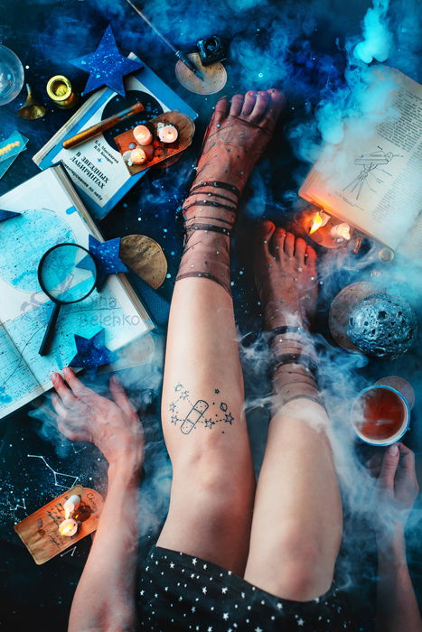 An overhead shot of a female models legs, sitting among candles, papers and other props