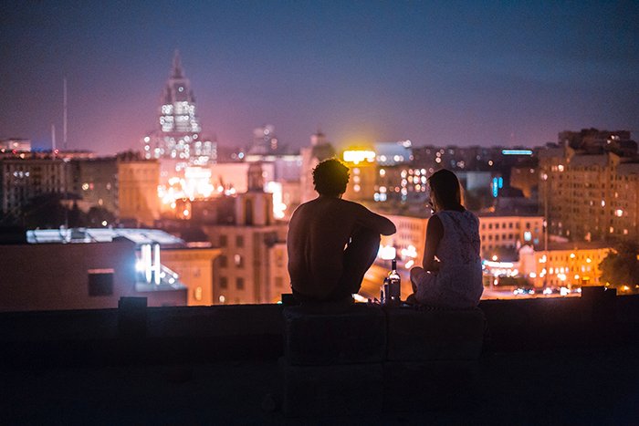 A candid photography example of a couple sitting on the roof of a tall building at night - 