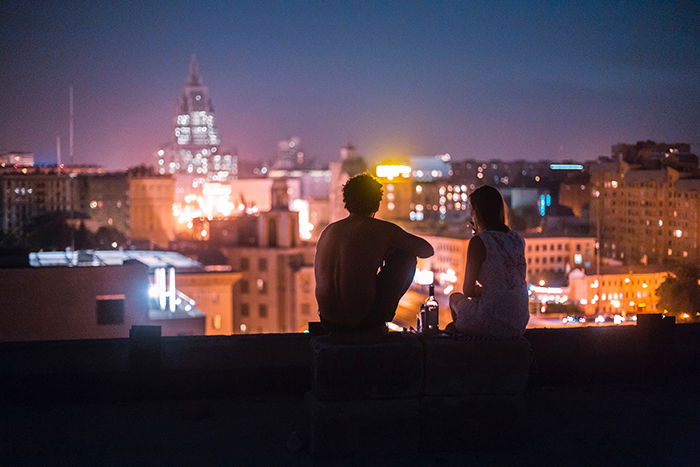 A candid photography example of a couple sitting on the roof of a tall building at night - 