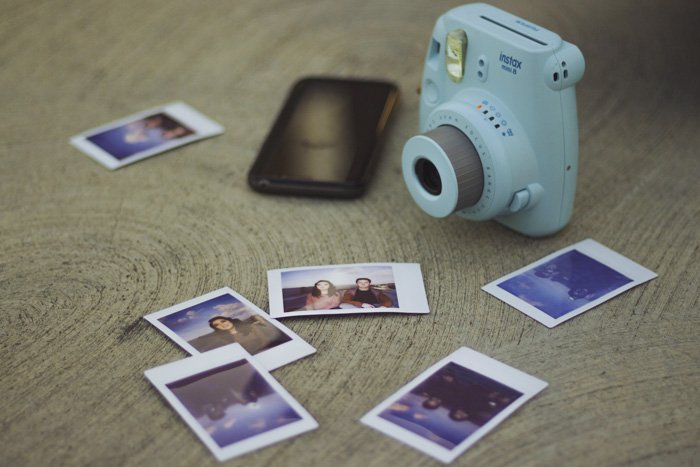 An instant camera and printed photos on a wooden table - DIY photo both ideas