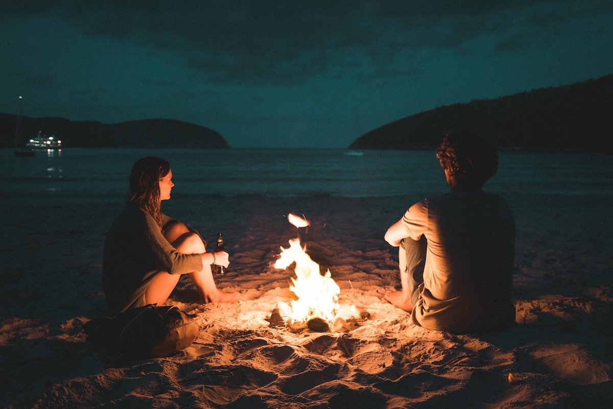 A couple sitting by a bonfire at a beach at night for fire photography