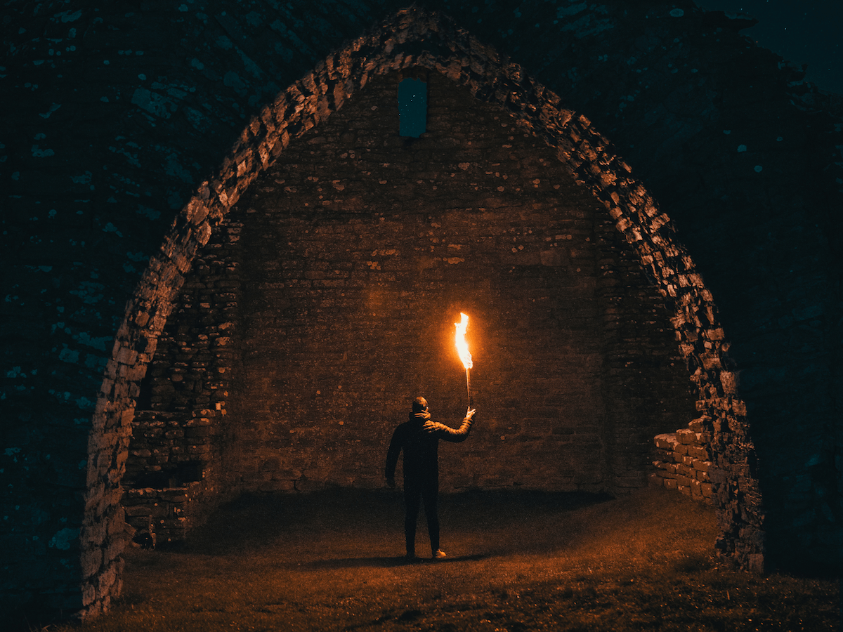 A person holding a fire torch under a stone arch for outdoor fire photography