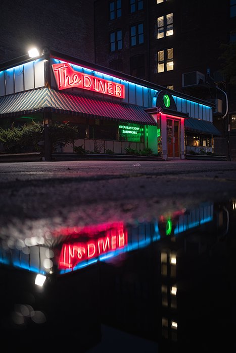 The red neon signs of a diner reflected in a puddle below - neon light photography