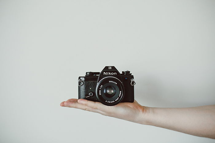 A Nikon Camera balanced on a persons outstretched hand - photography assignments