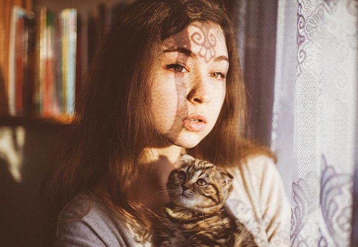 A portrait of a female model holding a cat by a window - photography projects