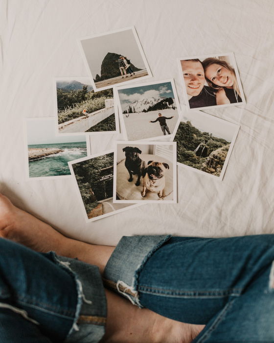 A close up of a person looking at 8 instant camera photos resting on a bed