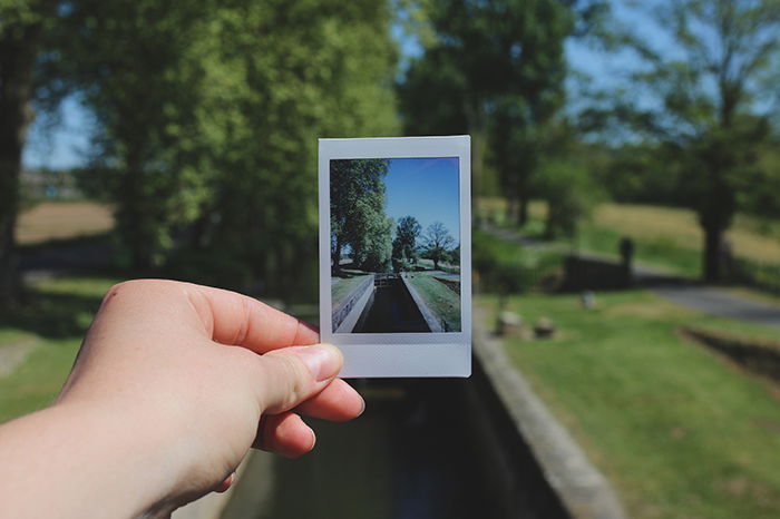 A hand holding a polaroid photo of a landscape withing a landscape 