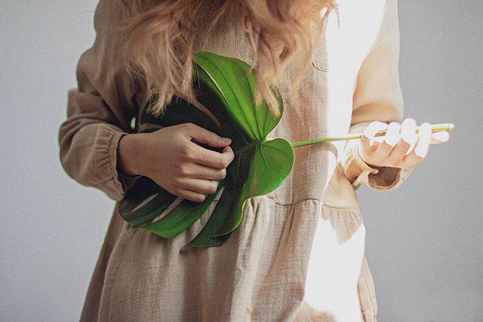 A close up portrait of a female model holding a large leaf as if it was a guitar she's playing