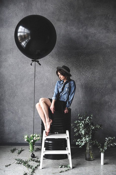 A female model posing by a large black balloon in a photography studio- photography internships