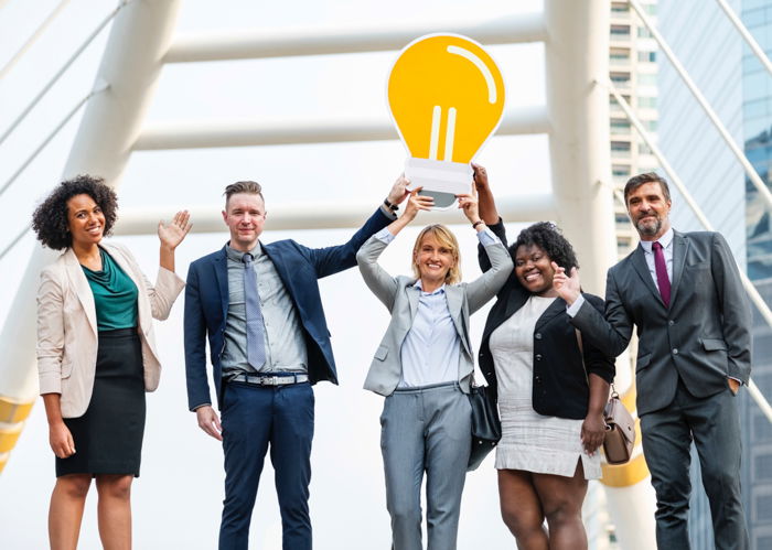 A group portrait of overly happy corporate office employees holding a cardboard lightbulb - business stock photos 