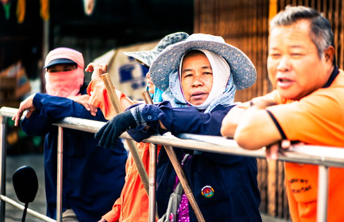 A street portrait of some of the clean up crew waiting behind the floats and participants during the annual flower parade in Chiang Mai, Thailand. Narrative photography tips